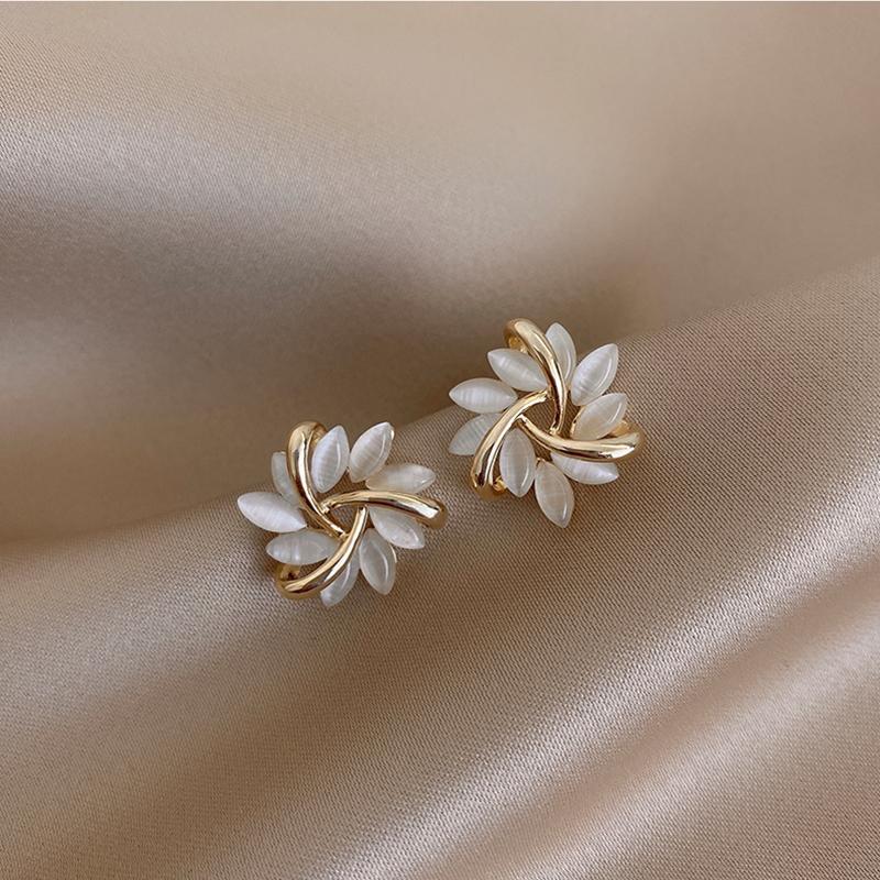 Paire de boucles d'oreilles puces florales avec pétales opalescents et finition dorée, posées sur un tissu soyeux beige, Maison Mercier.