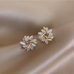 Paire de boucles d'oreilles puces florales avec pétales opalescents et finition dorée, posées sur un tissu soyeux beige, Maison Mercier.