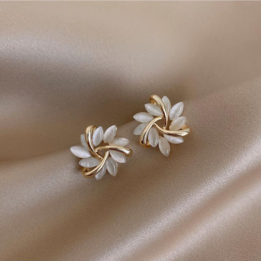 Paire de boucles d'oreilles puces florales avec pétales opalescents et finition dorée, posées sur un tissu soyeux beige, Maison Mercier.