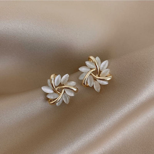Gros plan sur une boucle d'oreille puce florale, mettant en valeur les détails des pétales opalescents et la structure dorée entrelacée, Maison Mercier.