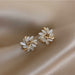 Gros plan sur une boucle d'oreille puce florale, mettant en valeur les détails des pétales opalescents et la structure dorée entrelacée, Maison Mercier.