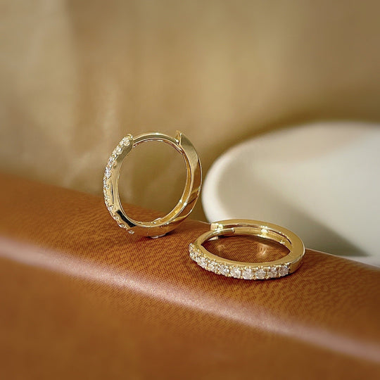 Détail d'une paire de créoles mini huggie en Argent 925 plaqué or, serties de zircons scintillants, posées sur un cuir patiné, Maison Mercier.