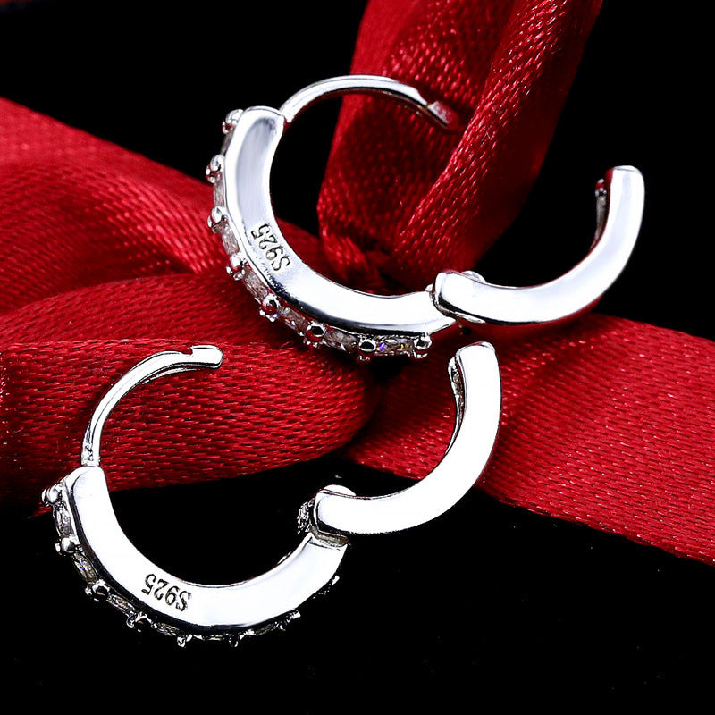 Paire de créoles mini huggie en Argent 925, estampillées 'S925', ouvertes et présentées sur un ruban de soie rouge, soulignant l'artisanat Maison Mercier.
