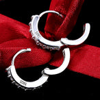 Paire de créoles mini huggie en Argent 925, estampillées 'S925', ouvertes et présentées sur un ruban de soie rouge, soulignant l'artisanat Maison Mercier.