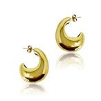 Vue rapprochée de boucles d'oreilles créoles sculpturales dorées, mettant en valeur leur forme courbée et leur éclat miroir.