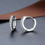 Détail d'une paire de créoles mini huggie en Argent 925 plaqué or, serties de zircons scintillants, posées sur un cuir patiné, Maison Mercier.
