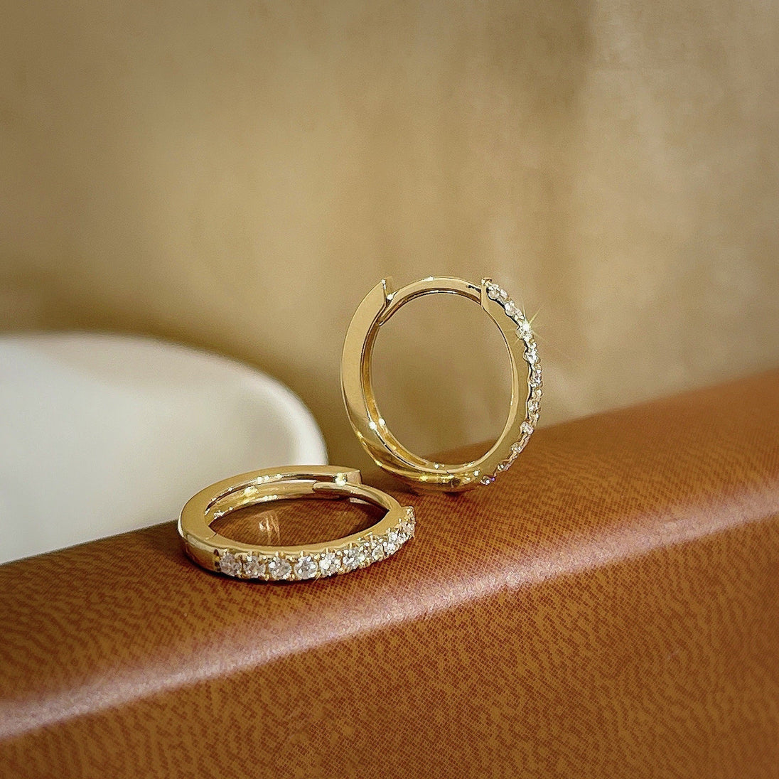 Vue rapprochée des créoles mini huggie dorées, révélant la finesse du sertissage des zircons et la brillance du métal précieux, Maison Mercier.