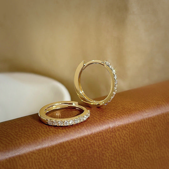 Vue rapprochée des créoles mini huggie dorées, révélant la finesse du sertissage des zircons et la brillance du métal précieux, Maison Mercier.