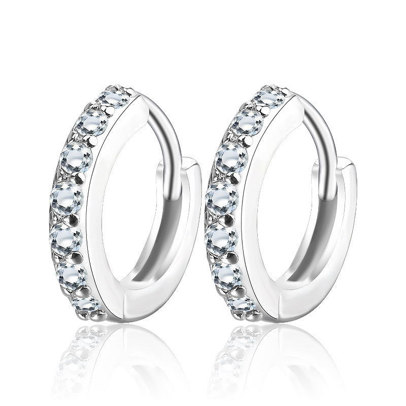 Détail d'une paire de créoles mini huggie en Argent 925 plaqué or, serties de zircons scintillants, posées sur un cuir patiné, Maison Mercier.