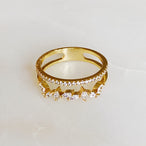 Vue de dessus d'une bague double rangée en plaqué or 18K, ornée de zircons ronds et marquises, sur un fond marbré clair, Maison Mercier.