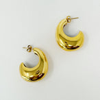 Détail d'une paire de boucles d'oreilles créoles bombées en acier doré poli, reflétant la lumière sur fond blanc.