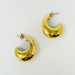 Détail d'une paire de boucles d'oreilles créoles bombées en acier doré poli, reflétant la lumière sur fond blanc.