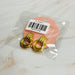 Détail de deux boucles d'oreilles anneaux entrelacés dorés en acier inoxydable poli sur un fond de marbre clair, Maison Mercier.