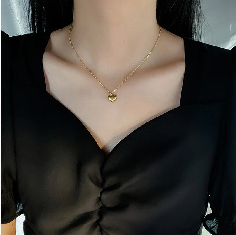 Vue rapprochée d'un collier pendentif cœur 'Love' doré porté par une femme, mettant en valeur la délicatesse du bijou et de la chaîne, Maison Mercier.