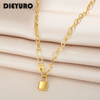 Collier gourmette ovale doré avec cadenas et épingle 'Love' en acier inoxydable, logo DIEURO en haut à gauche, sur un tissu soyeux beige, Maison Mercier.
