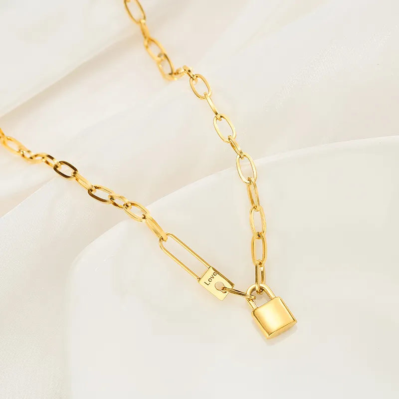 Gros plan sur le cadenas et l'épingle 'Love' du collier gourmette ovale doré, mettant en valeur la gravure délicate, Maison Mercier.