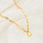 Gros plan sur le cadenas et l'épingle 'Love' du collier gourmette ovale doré, mettant en valeur la gravure délicate, Maison Mercier.