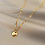 Détail d'un collier pendentif cœur 'Love' en acier inoxydable doré poli, posé sur un tissu élégant, Maison Mercier.