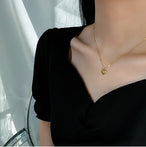 Collier pendentif cœur 'Love' en acier inoxydable doré porté avec élégance sur le décolleté d'une femme en robe noire, Maison Mercier.