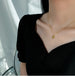 Collier pendentif cœur 'Love' en acier inoxydable doré porté avec élégance sur le décolleté d'une femme en robe noire, Maison Mercier.