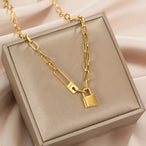 Détail d'un collier gourmette ovale doré avec cadenas et épingle 'Love' sur un écrin beige, Maison Mercier.