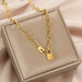 Détail d'un collier gourmette ovale doré avec cadenas et épingle 'Love' sur un écrin beige, Maison Mercier.