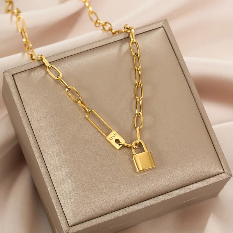 Détail d'un collier gourmette ovale doré avec cadenas et épingle 'Love' sur un écrin beige, Maison Mercier.