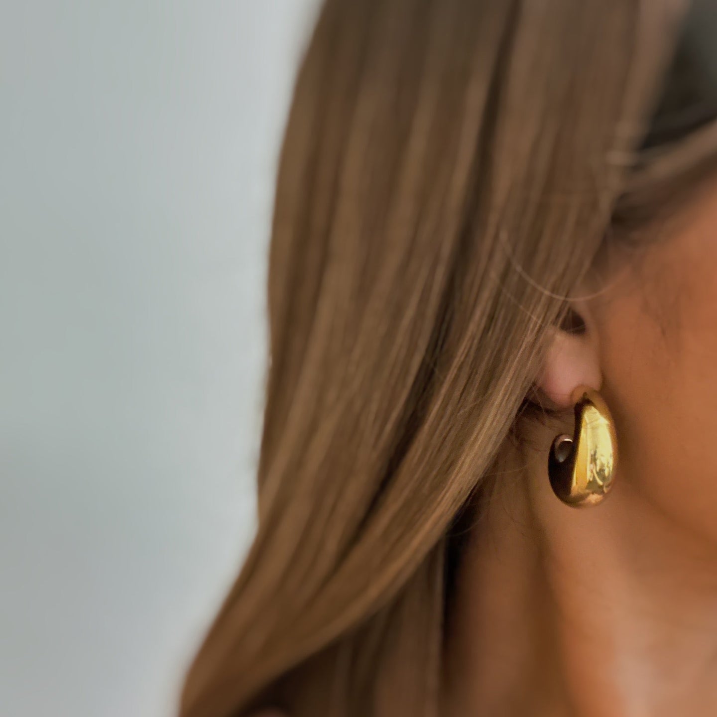 Détail d'une paire de boucles d'oreilles créoles bombées en acier doré poli, reflétant la lumière sur fond blanc.
