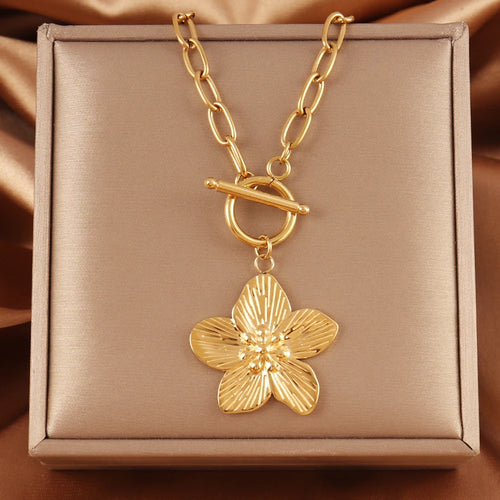 Collier chaîne ovale en acier inoxydable doré, avec pendentif fleur sculptée et fermoir T-Bar, présenté sur un écrin beige satiné, Maison Mercier.