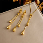 Parure Goutte d'Eau en acier doré, collier lariat et boucles pendantes, présentée sur un fond élégant et texturé, Maison Mercier.