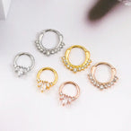 Gros plan sur un piercing clicker septum en acier chirurgical or rose orné de zircons taille marquise, avec un détail de goutte scintillante, Maison Mercier.