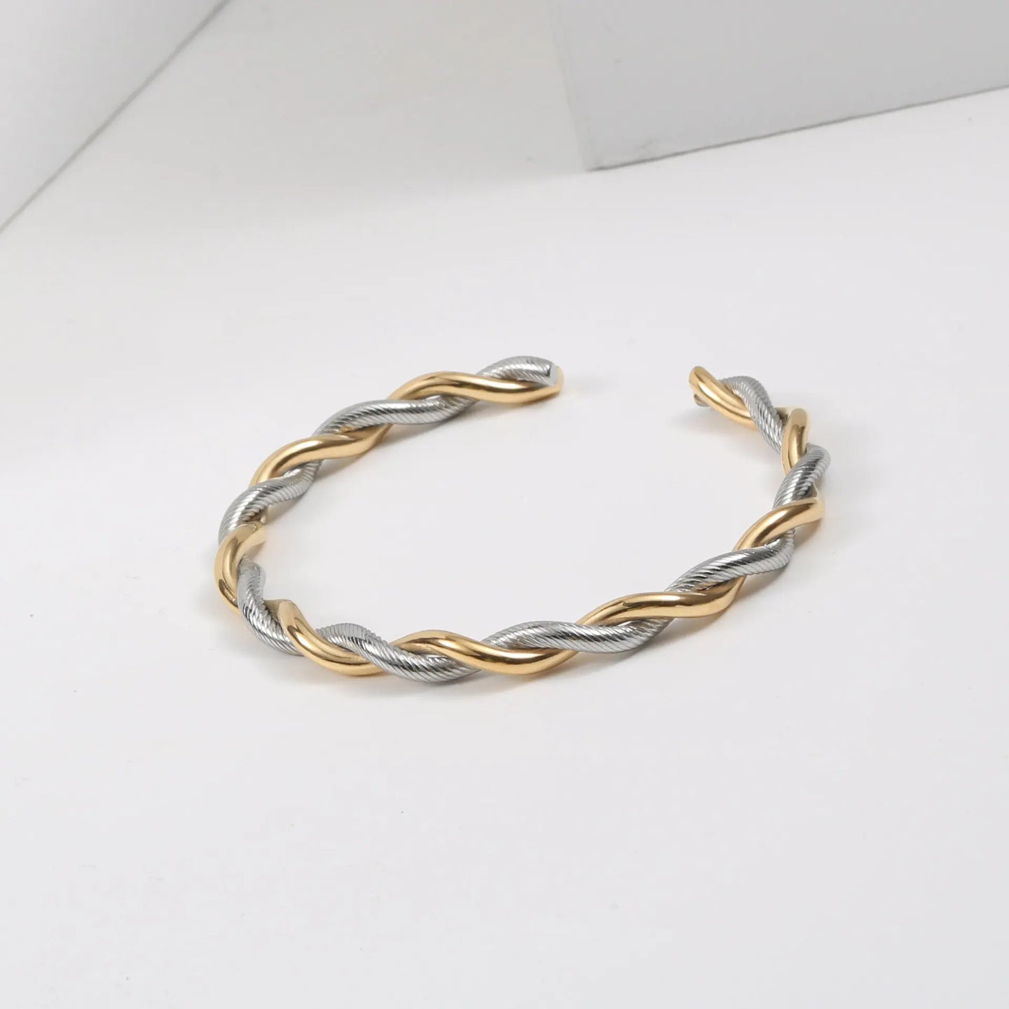 Bracelet jonc ouvert torsadé doré en acier inoxydable, présenté dans un écrin de velours rouge, avec une étiquette Saint Laurent et une carte Joyful Nails Studio.