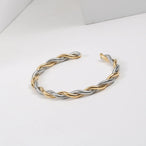 Bracelet jonc ouvert torsadé doré en acier inoxydable, présenté dans un écrin de velours rouge, avec une étiquette Saint Laurent et une carte Joyful Nails Studio.