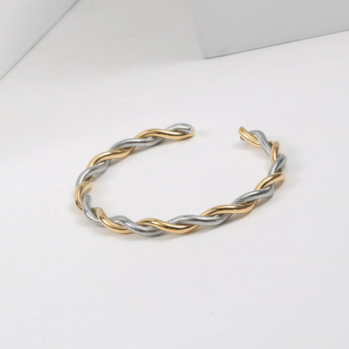 Bracelet jonc ouvert torsadé doré en acier inoxydable, présenté dans un écrin de velours rouge, avec une étiquette Saint Laurent et une carte Joyful Nails Studio.