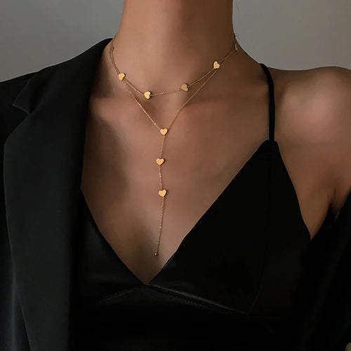 Détail d'un collier pendentif cœur 'Love' en acier inoxydable doré poli, posé sur un tissu élégant, Maison Mercier.