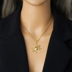 Détail d'un collier pendentif soleil rayonnant en acier inoxydable doré, présenté sur un écrin beige, Maison Mercier.