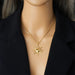 Détail d'un collier pendentif soleil rayonnant en acier inoxydable doré, présenté sur un écrin beige, Maison Mercier.