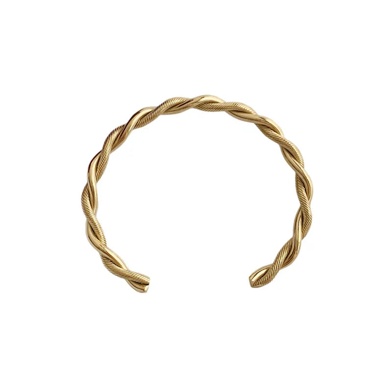 Bracelet jonc ouvert torsadé doré en acier inoxydable, présenté dans un écrin de velours rouge, avec une étiquette Saint Laurent et une carte Joyful Nails Studio.