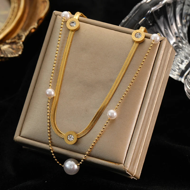 Gros plan sur un collier multi-rangs doré en acier inoxydable, composé d'une chaîne à billes et d'une chaîne serpent, agrémenté de perles blanches et de pendentifs ronds sertis de zirconiums.