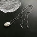 Collier pendentif ovale sculptural poli en finition argentée, posé sur une surface sombre à côté d'un élément décoratif en verre texturé, Maison Mercier.