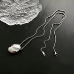 Deux colliers pendentifs ovales sculpturaux polis, l'un en finition argentée et l'autre en finition dorée, posés sur un tissu soyeux, Maison Mercier.