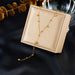 Détail d'un collier Lariat Y en acier inoxydable doré, orné de sphères polies, présenté sur un écrin beige.