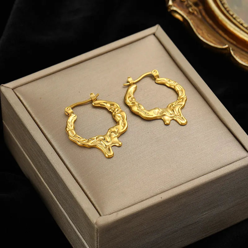 Détail d'une paire de boucles d'oreilles créoles dorées à la texture organique et fondue, Maison Mercier.