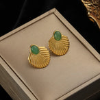 Gros plan d'une paire de boucles d'oreilles créoles dorées à la texture fondue et irrégulière, posées sur un écrin beige, Maison Mercier.