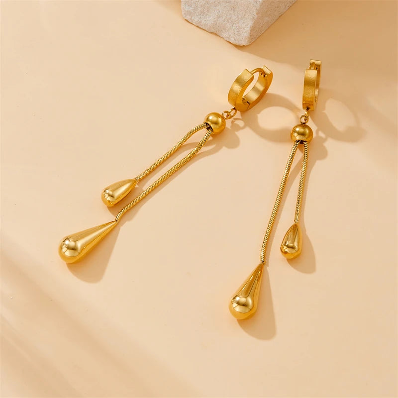 Parure Goutte d'Eau en acier doré, collier lariat et boucles pendantes, présentée sur un fond élégant et texturé, Maison Mercier.