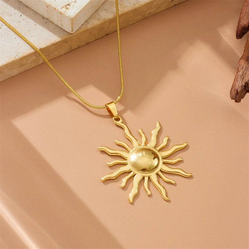 Détail d'un collier pendentif soleil rayonnant en acier inoxydable doré, présenté sur un écrin beige, Maison Mercier.
