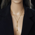 Parure Goutte d'Eau en acier doré, collier lariat et boucles pendantes, présentée sur un fond élégant et texturé, Maison Mercier.