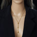 Parure Goutte d'Eau en acier doré, collier lariat et boucles pendantes, présentée sur un fond élégant et texturé, Maison Mercier.