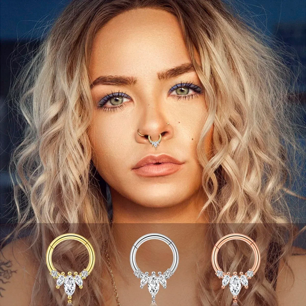Gros plan sur un piercing clicker septum en acier chirurgical doré orné de zircons ronds en arc de cercle, avec une pierre centrale et une goutte, Maison Mercier.
