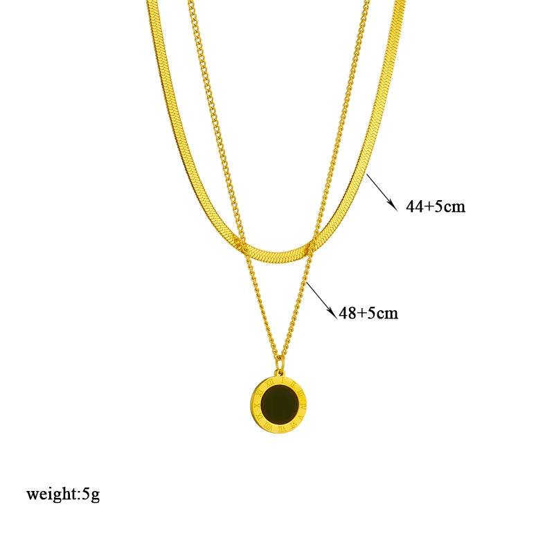 Quatre colliers dorés en acier inoxydable, présentant des pendentifs variés : un cercle noir, un cœur vert, un cœur avec une pampille noire, et un ensemble de chaînes avec étoiles et un pendentif carré bleu, présentés sur des supports beiges.